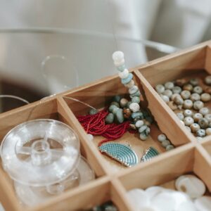 Wooden container with abundance of colorful beads and elastic cord for making bracelet placed on glass table in light room