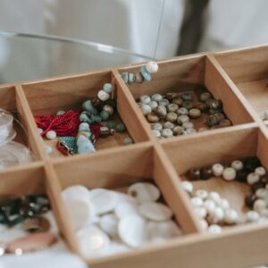 Wooden container with collection of different colorful beads for making handmade bracelets placed on table in light room at home