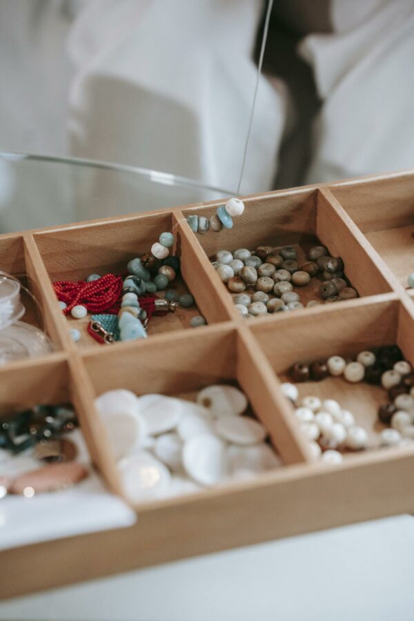 Wooden container with collection of different colorful beads for making handmade bracelets placed on table in light room at home